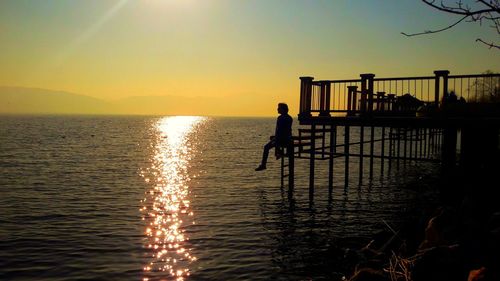 Silhouette boy playing in sea against sky during sunset