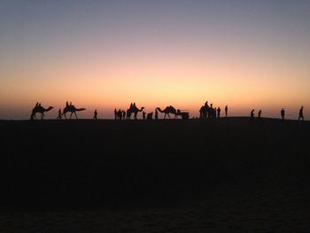 Silhouette people and camels at desert during sunset