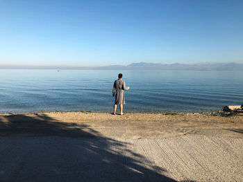 Rear view of man standing on beach against sky