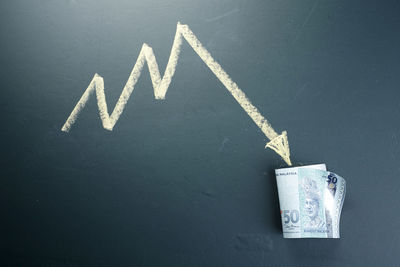 Close-up of arrow symbol with paper currency on table