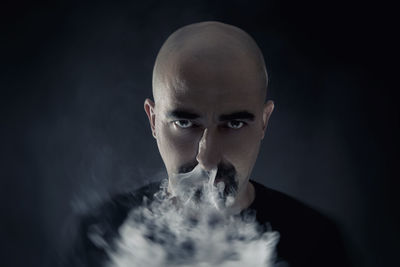 Portrait of mature man smoking cigarette against black background