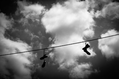 Low angle view of shoes hanging on wire against cloudy sky