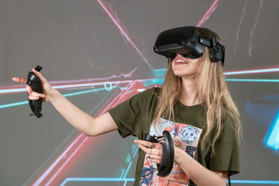 Portrait of young woman with arms raised standing against wall