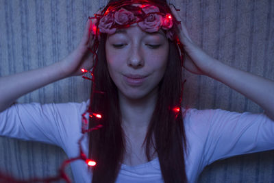 Woman with illuminated string lights against wall