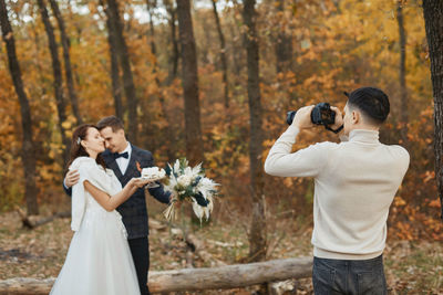 Rear view of woman photographing while standing against trees