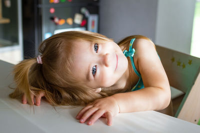 Adorable baby girl with blond hair and blue eyes with hand on table. sunny morning at home.