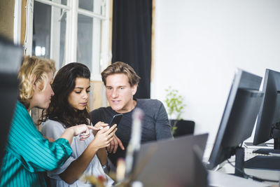 Programmers looking at female computer hacker using smart phone at desk in office