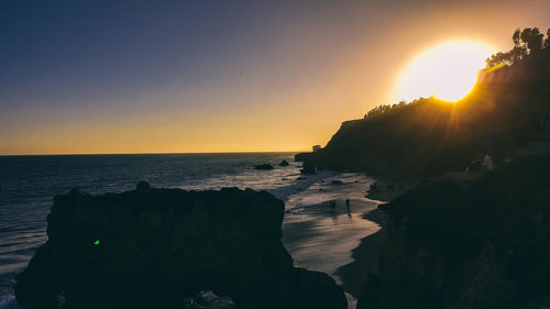 Scenic view of sea and silhouette rock formations against sky during sunset