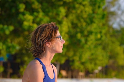 Portrait of young woman looking away against trees