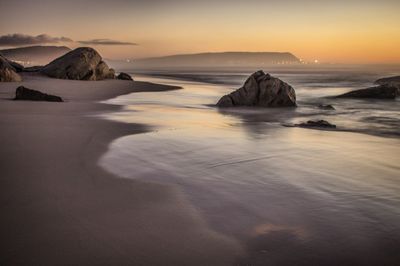 Rocks on beach against sky during sunset