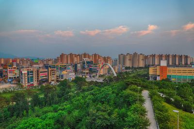 Trees and buildings in city against sky during sunset