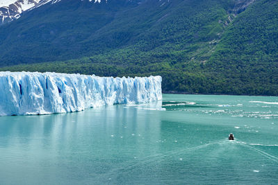 Blue ice of perito moreno glacier, patagonia, with tourist boat on turquoise water of lago argentino