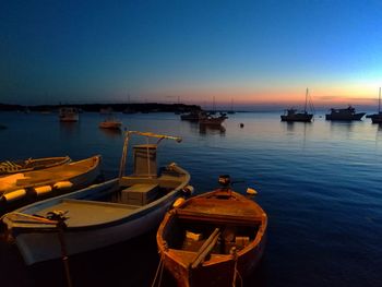 Boats moored in harbor at sunset