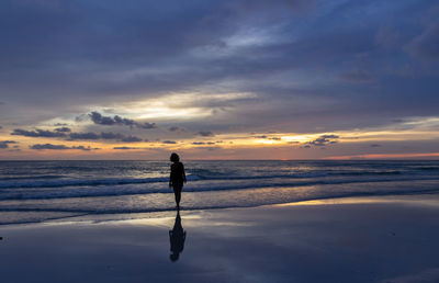 Silhouette woman standing on beach against sky during sunset