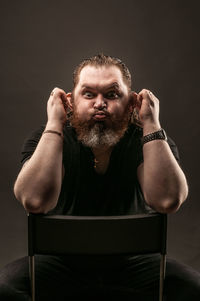 Portrait of man sitting against black background