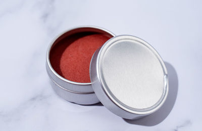 Red lip balm in round tin case on light background with shadow overlay, mockup design, label