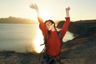 Midsection of woman with arms raised against sky during sunset