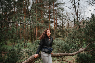 Portrait of young woman standing by trees in forest
