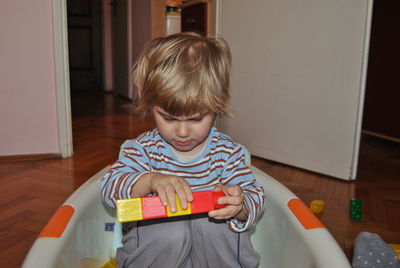 Cute boy sitting while playing with blocks at home