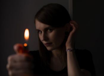 Portrait of young woman holding candles against black background