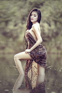 Portrait of young woman standing against lake in forest