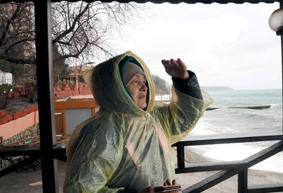 Portrait of an elderly woman in a raincoat walking in the rain. she looks at the sea on a rainy day.