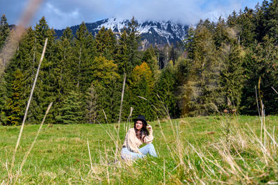 Woman sitting on field against trees in forest
