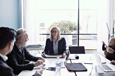 Smiling businesswoman discussing with colleagues at conference table in board room