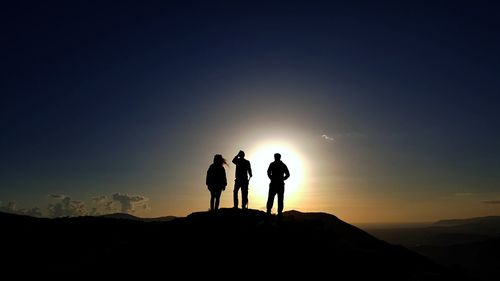 Silhouette of people standing on landscape at sunset