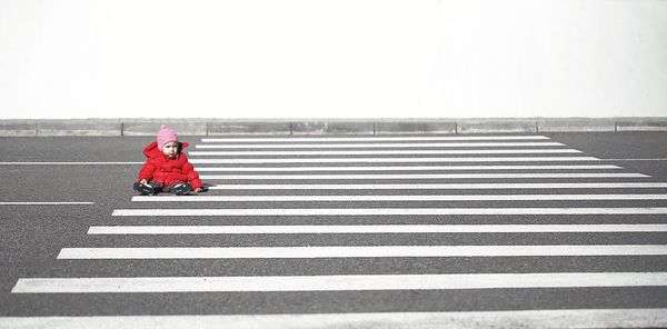 Baby sitting on zebra crossing against clear sky