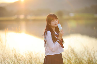 Young woman standing against lake during sunset