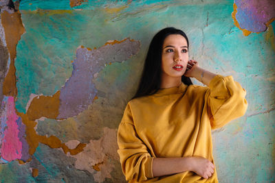 Portrait of beautiful young woman standing against colorful wall