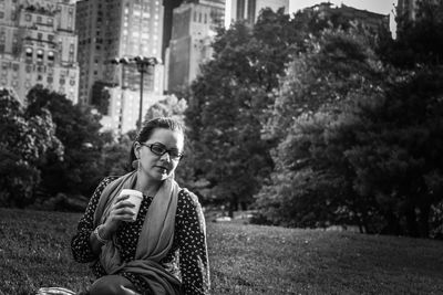 Young woman holding drink while sitting on grassy field at park