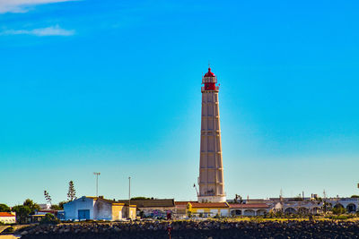 Lighthouse by buildings against blue sky