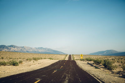 Road amidst field against clear blue sky