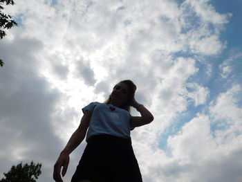 Low angle view of woman standing against cloudy sky