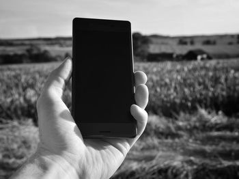 Cropped hand of man holding mobile phone against grassy field