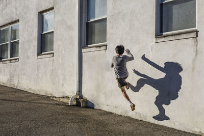 Rear view of teenage boy jumping over wall during sunny day