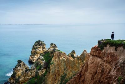 Man standing on cliff by sea