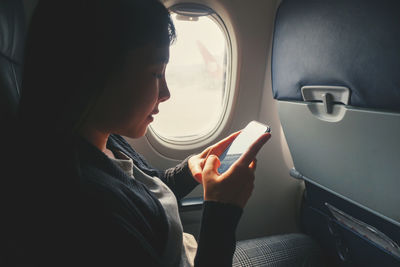 Young woman using mobile phone while sitting in airplane