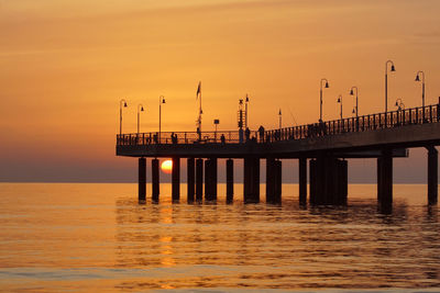 Silhouette pier over sea against orange sky