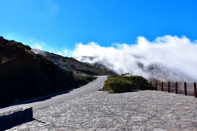 Empty road by mountain against blue sky