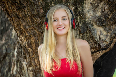 Portrait of smiling young woman against tree trunk