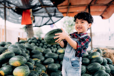 Smiling boy holding watermelons while standing outdoors