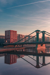 Bridge over river by buildings against sky during sunset