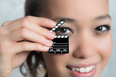 Portrait of woman holding little clapperboard while standing against wall