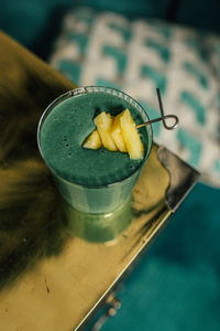 Green spirulina smoothie with pineapple on brass, gold table and teal background