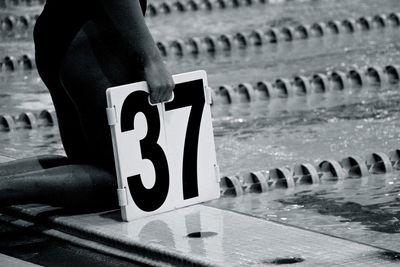 Midsection of woman holding number 37 while kneeling at pool