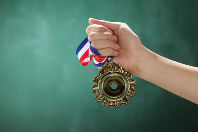 Cropped hand of woman holding medal against wall