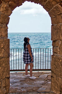 Woman looking up while standing by railing against sea